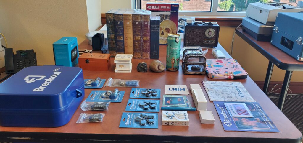 Picture 4 - Some of the Purchased EER Materials and Probs  - a table with a lot of game paraphernalia on it, including the breakout EDU case and some books