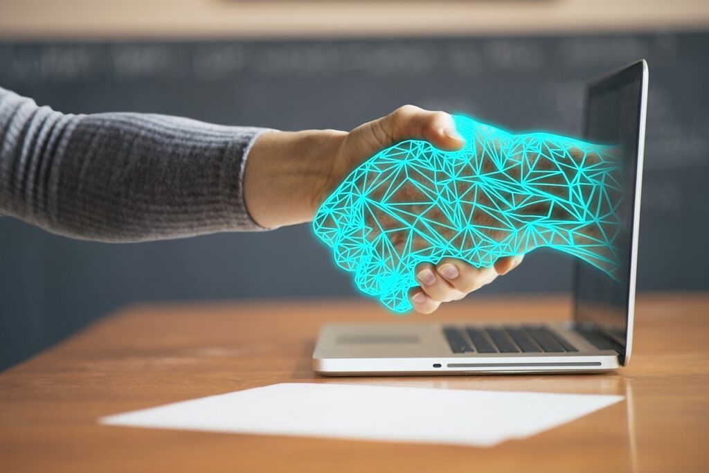 a hand reaching out through a computer and shaking the hand of the person at the computer