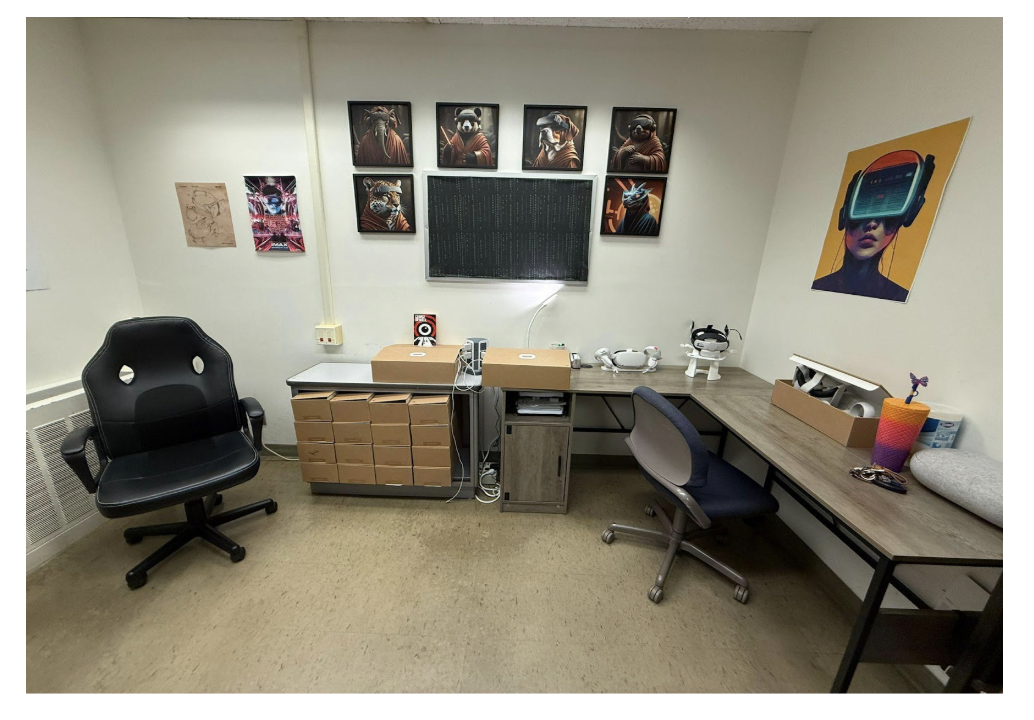 Picture 5 - VR Lab at the university - has several tables, two chairs, a storage space for headsets, a monitor, and some art related to VR